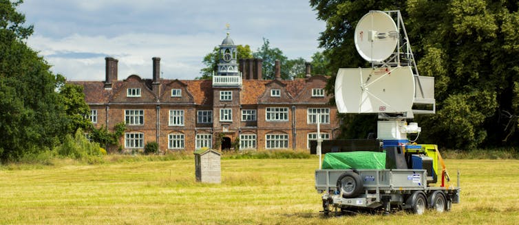 A radar machine in front of a field and a large building.