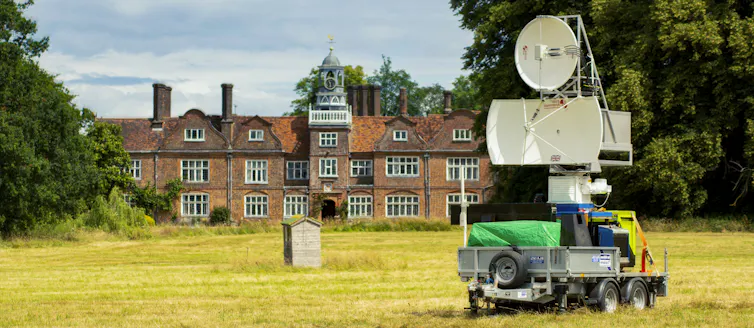 A radar machine in front of a field and a large building.