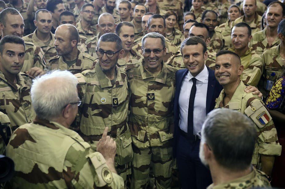  A man wearing a suit, tie and shirt poses with several soldiers in military fatigues.