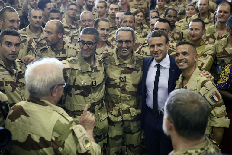 A man wearing a suit, tie and shirt poses with several soldiers in military fatigues.