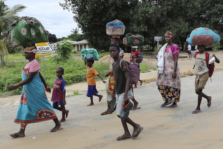 Women and children carry their meagre possessions wrapped in clothes on their heads.
