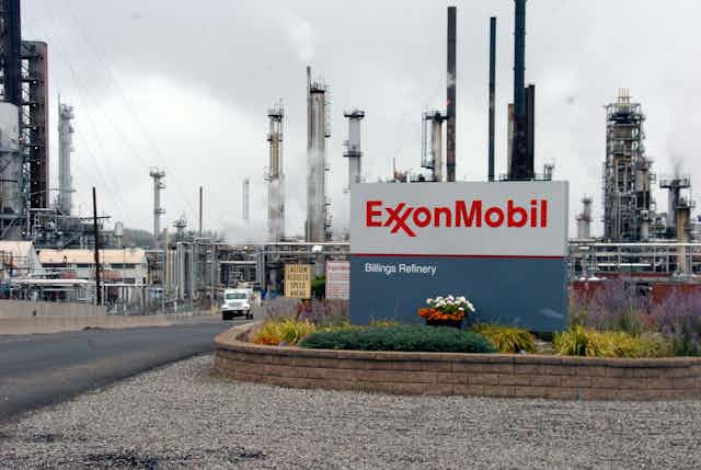 An Exxon Mobil sign sits in front of its Billings Refinery in Billings, Mont., with smoke stacks in the background. 