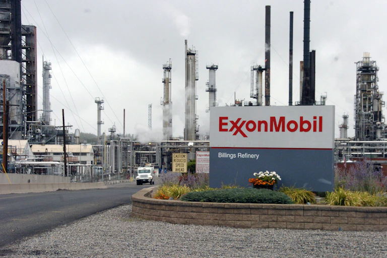 An Exxon Mobil sign sits in front of its Billings Refinery in Billings, Mont., with smoke stacks in the background.