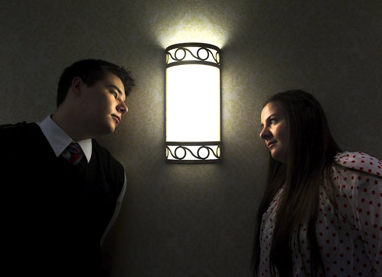 Teenage boy and teenage girl look at each in front of a light