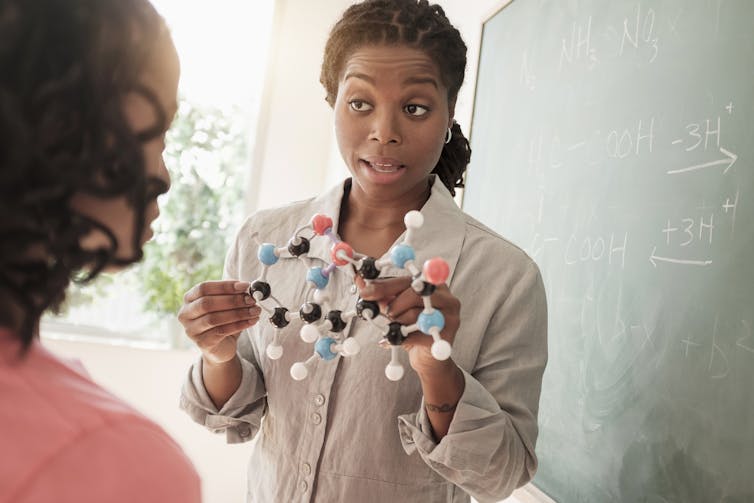 A science teacher holds up a model of a molecule to a student.