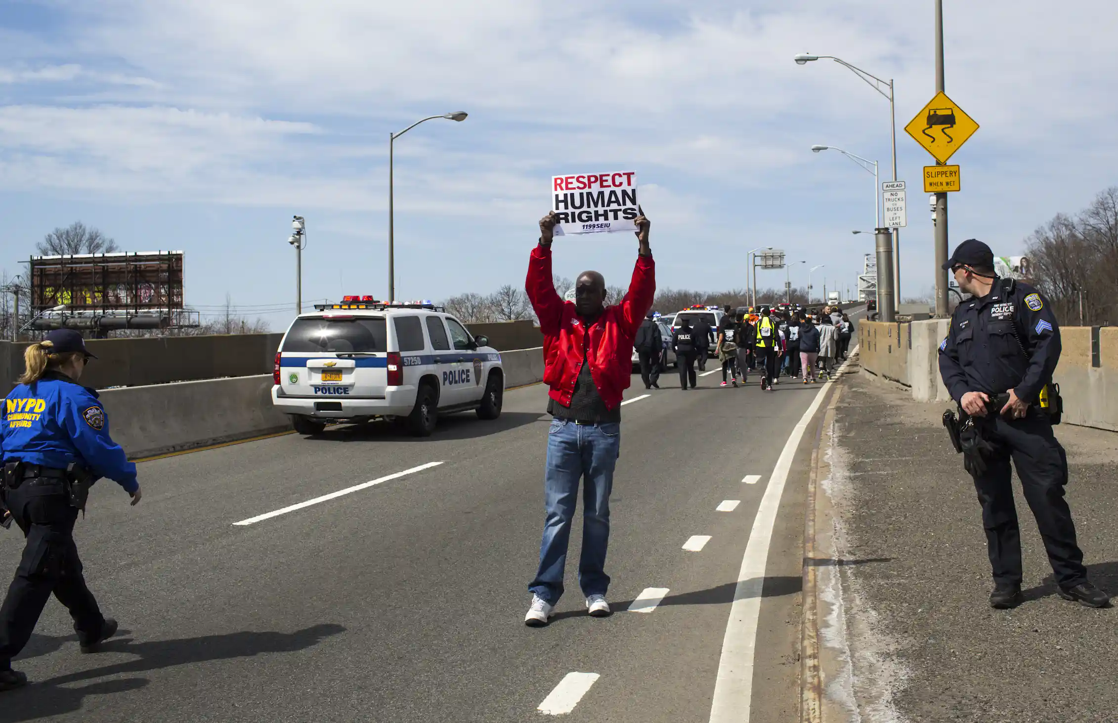 A man holding up a sign 'RESPECT HUMAN RIGHTS' as two police officers stand near him and approaching marchers.