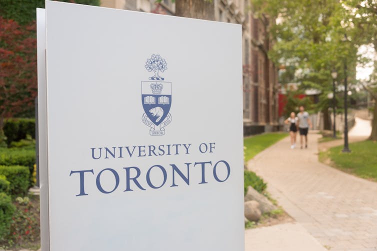 A sign for the University of Toronto in front of a footpath.