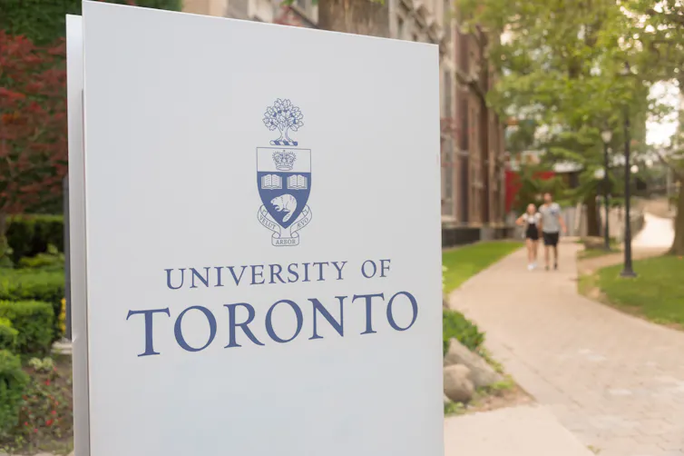 A sign for the University of Toronto in front of a footpath.