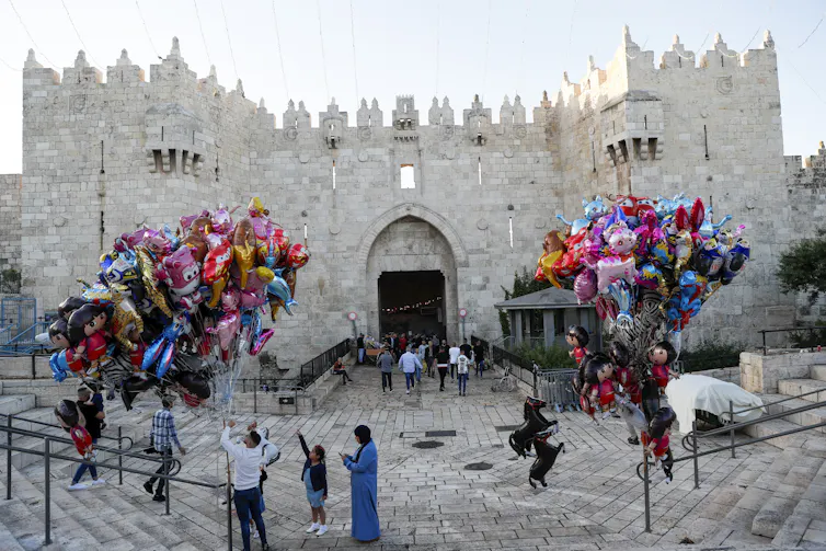 Palestinians make their way to attend Eid al-Fitr prayers at Al Aqsa mosque in Jerusalem’s old city, while children play with balloons in the street outside, May 13 2021.