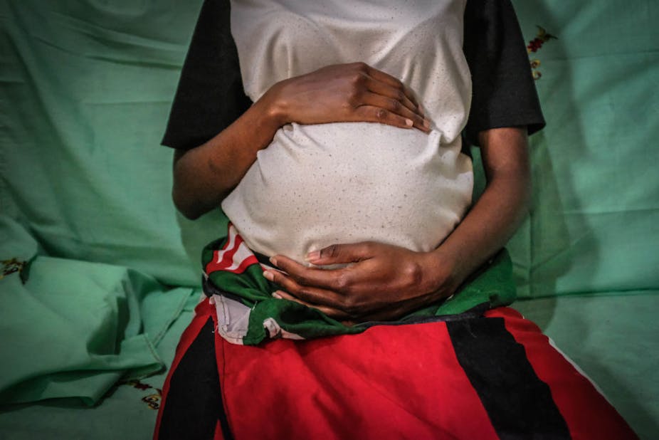 A young Kenyan mother holds her baby bump.