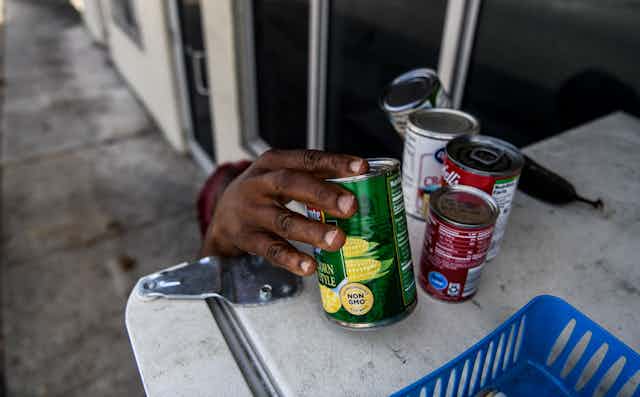 A woman reaches out to pick up cans of food at a community refrigerator in Miami.