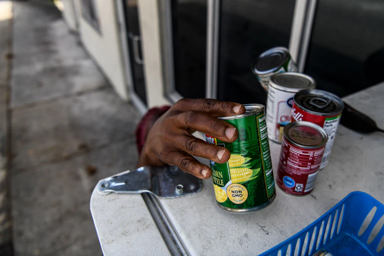 A woman reaches out to pick up cans of food at a community refrigerator in Miami.
