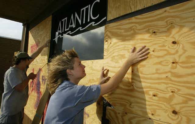 A man and woman put plywood over a store's windows