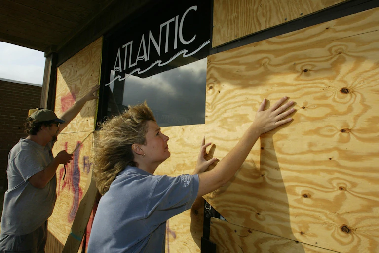A man and woman put plywood over a store's windows