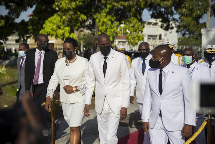 Le président haïtien Moise et son épouse marchent en compagnie d’un homme, tous vêtus de blanc