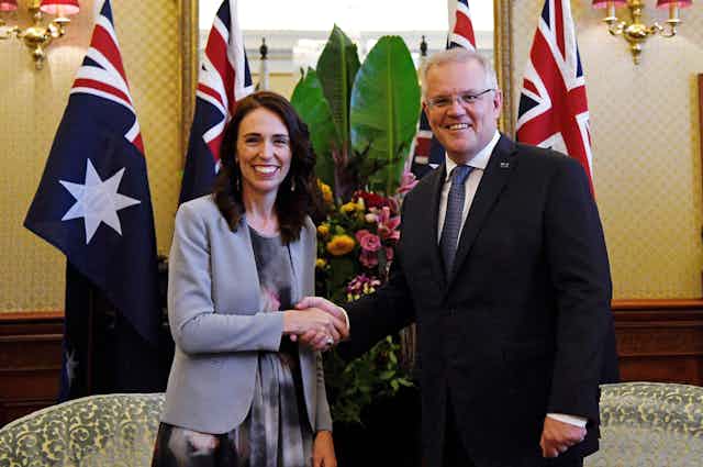 Jacinda Ardern and Scott Morrison shaking hands with flags in the background