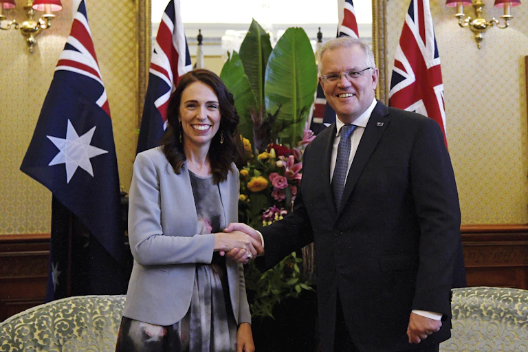 Jacinda Ardern and Scott Morrison shaking hands with flags in the background