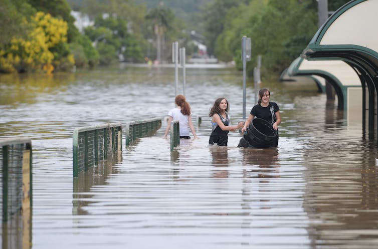 Three girls wade through floodwaters