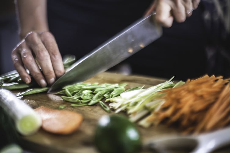 Um cozinheiro cortando legumes em uma tábua.