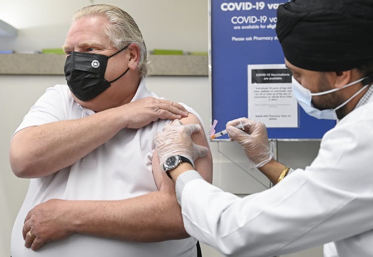Doug Ford in a T-shirt and face mask, with his sleeve rolled up, getting vaccinated