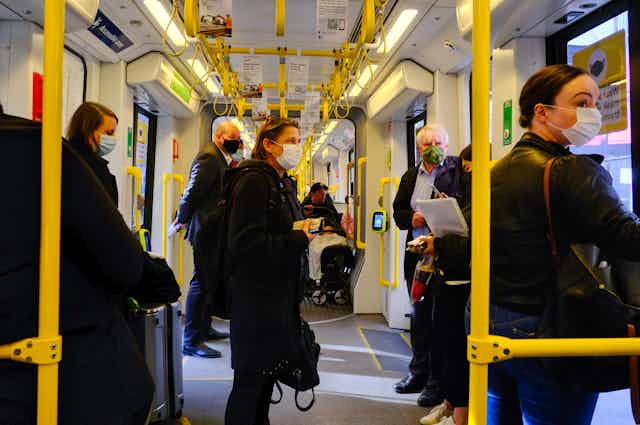 People in masks travel on a tram.