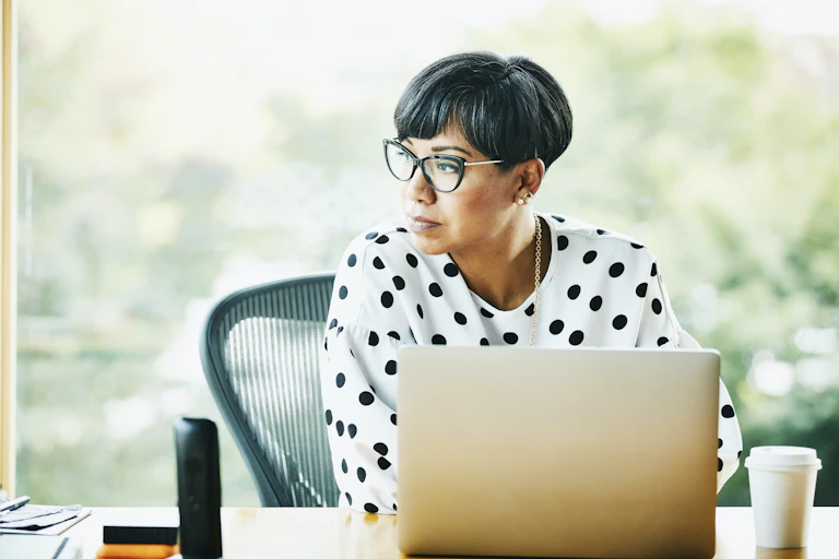 woman at laptop pensively looks off into distance