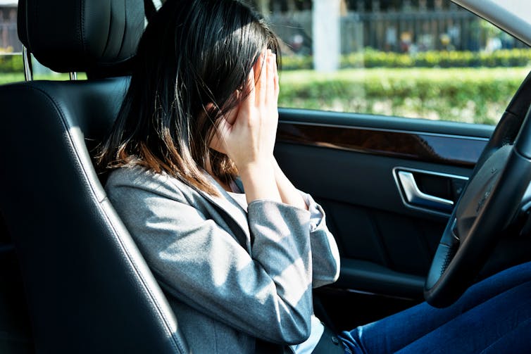 woman in a car's driver's seat covers her face with her hands