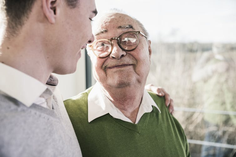 older man smiles up at younger man with his arm around his shoulders