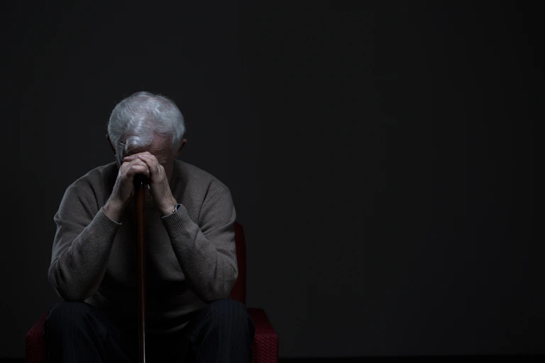 Older man holds head on hands over walking stick