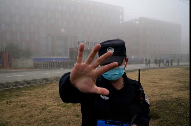 Gardien de sécurité lève la main pour empêcher des gens d'entrer dans le périmètre de sécurité de l'Institut de virologie de Wuhan (WIV