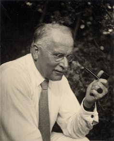 Black and white photo of older man wearing a tie and holding a pipe.