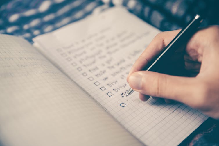 Hand using pen to write checklist on notebook.