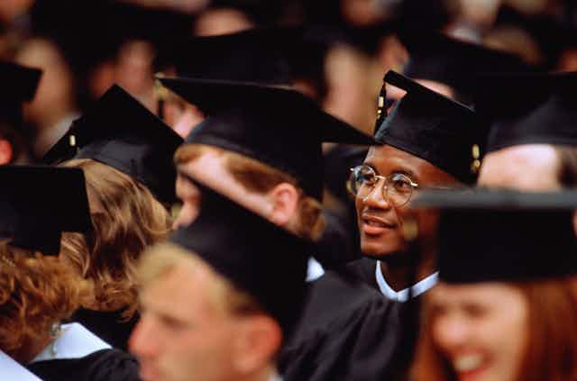 A Black student sits at his college graduation among his classmates.