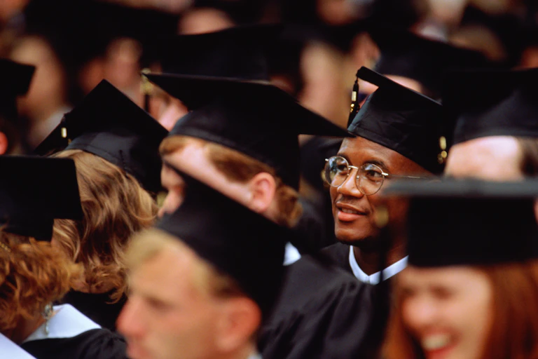 A Black student sits at his college graduation among his classmates.