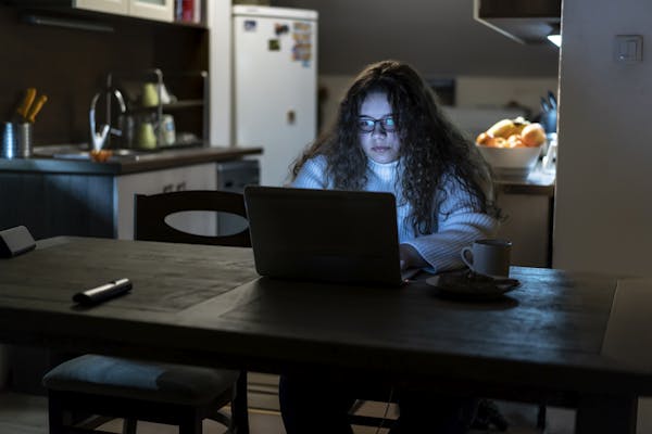 A young girl is working on her laptop late at night.