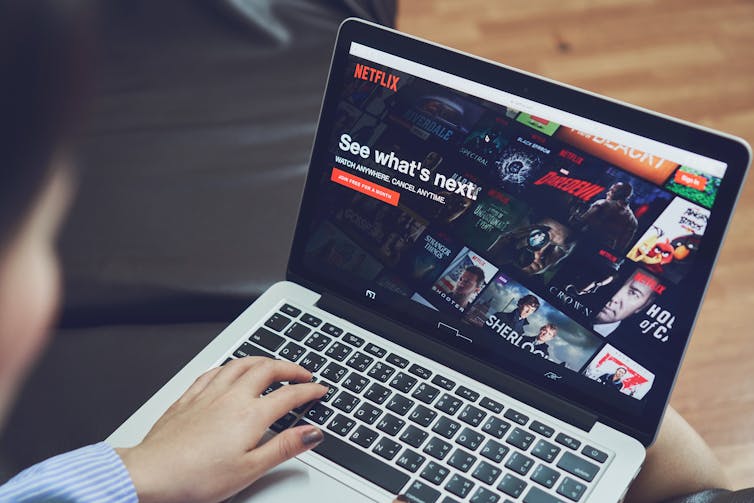 A young woman at her computer looks at the Netflix menu to choose a movie