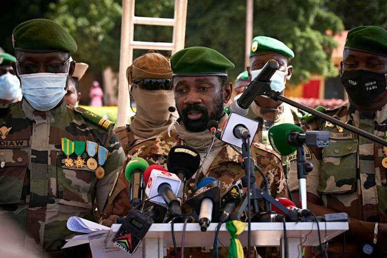 Men in military uniforms stand at a podium facing microphones