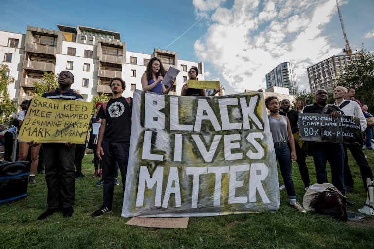 Protestors gathered together on a lawn holding up protest signs that say Black Lives Matter, Sarah Reed, Mzee Mohammed, Jermaine Baker, Mark Duggan and Independent Police Complaints Commission 80 per cent ex-police
