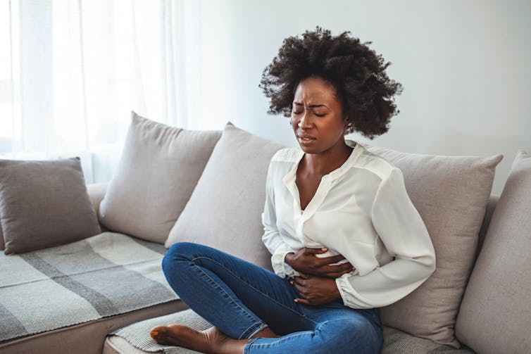 A woman sits on a sofa holding her stomach in pain