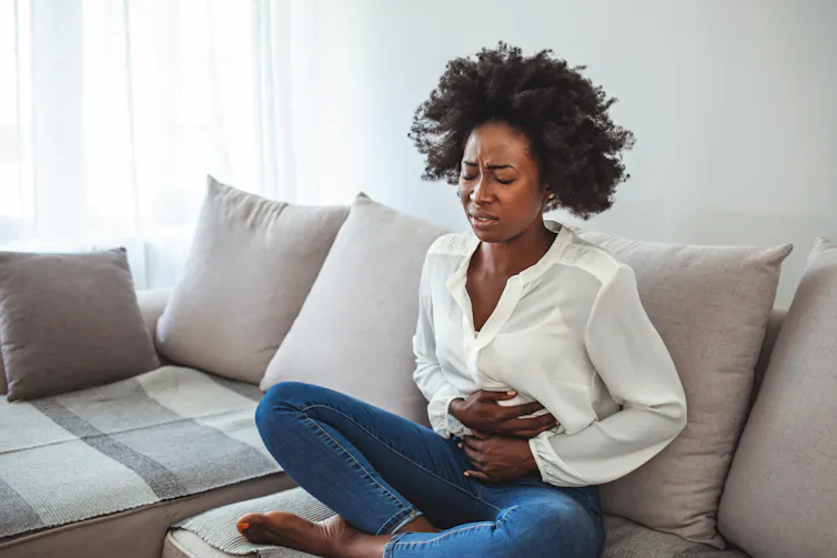 A woman sits on a sofa holding her stomach in pain