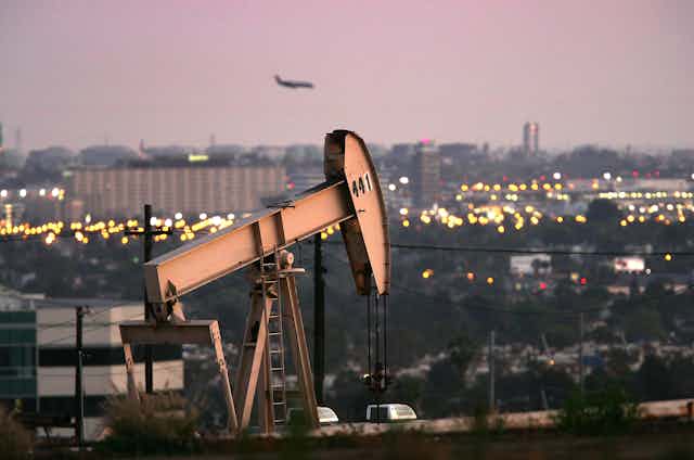 Oil well on a hill near an airport and office buildings, with a plane landing.