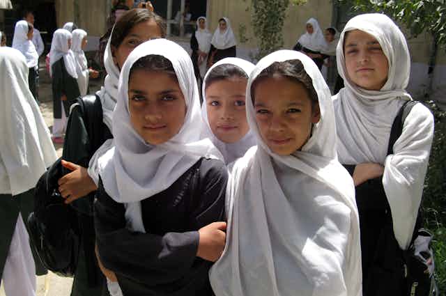 A row of five school girls wearing white hijabs.
