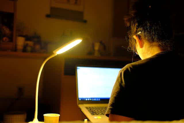 Woman working at laptop lit by desktop lamp at night