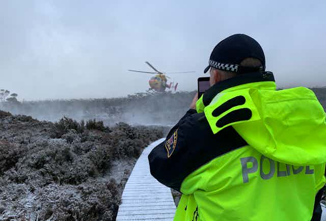 Police officer looks at a helicopter on a wintery trail