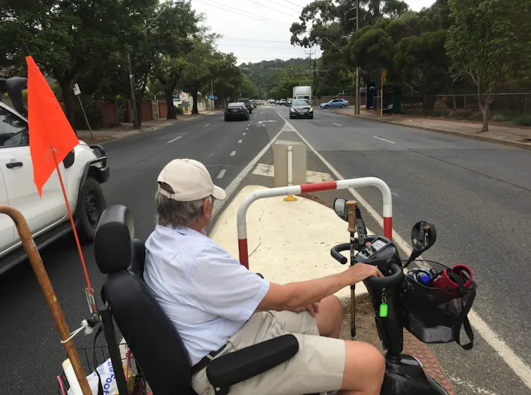Man on mobility scooter waits in the middle of the road for traffic to pass so he can cross