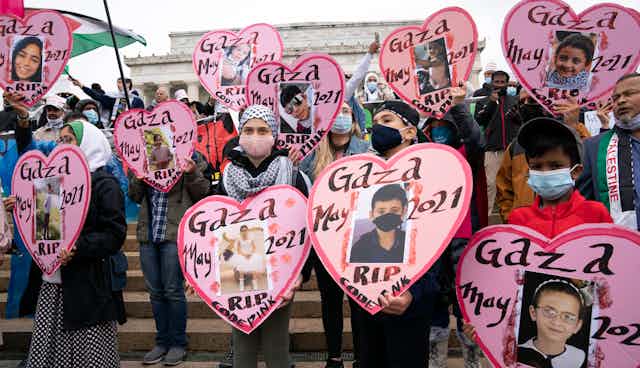 Children demonstrators wearing face masks hold heart shaped pictures of children killed that say Gaza May RIP. 