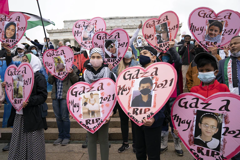 Children demonstrators wearing face masks hold heart shaped pictures of children killed that say Gaza May RIP.