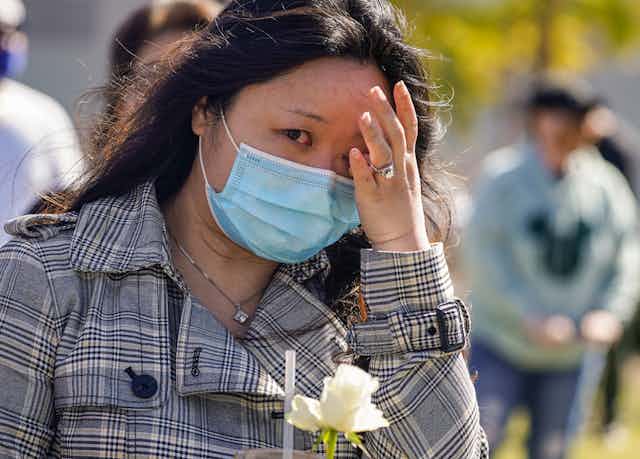 Une femmes asiatique, portant un masque, pleure durant une manifestation