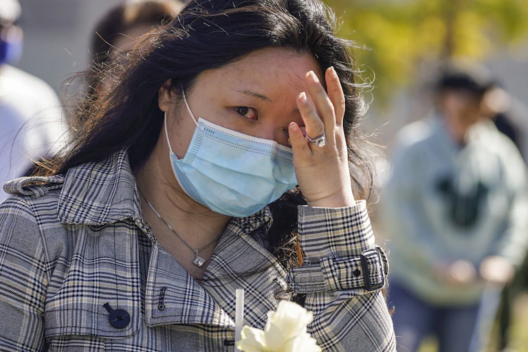 Une femmes asiatique, portant un masque, pleure durant une manifestation