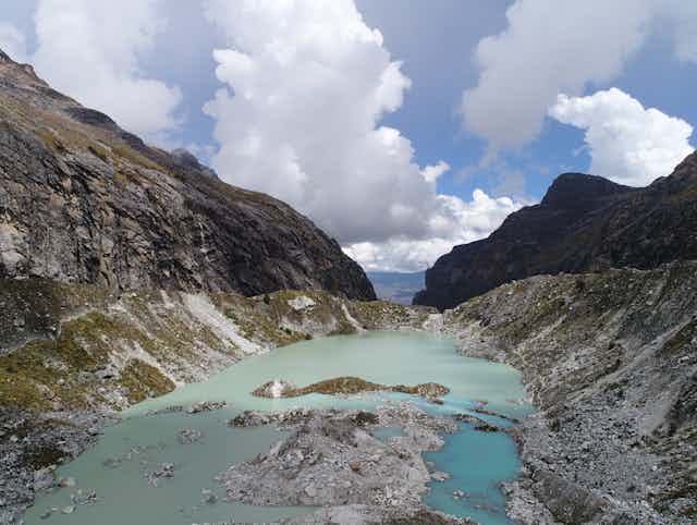 Aerial view of glacial lake with rocky slope, looking into a valley 